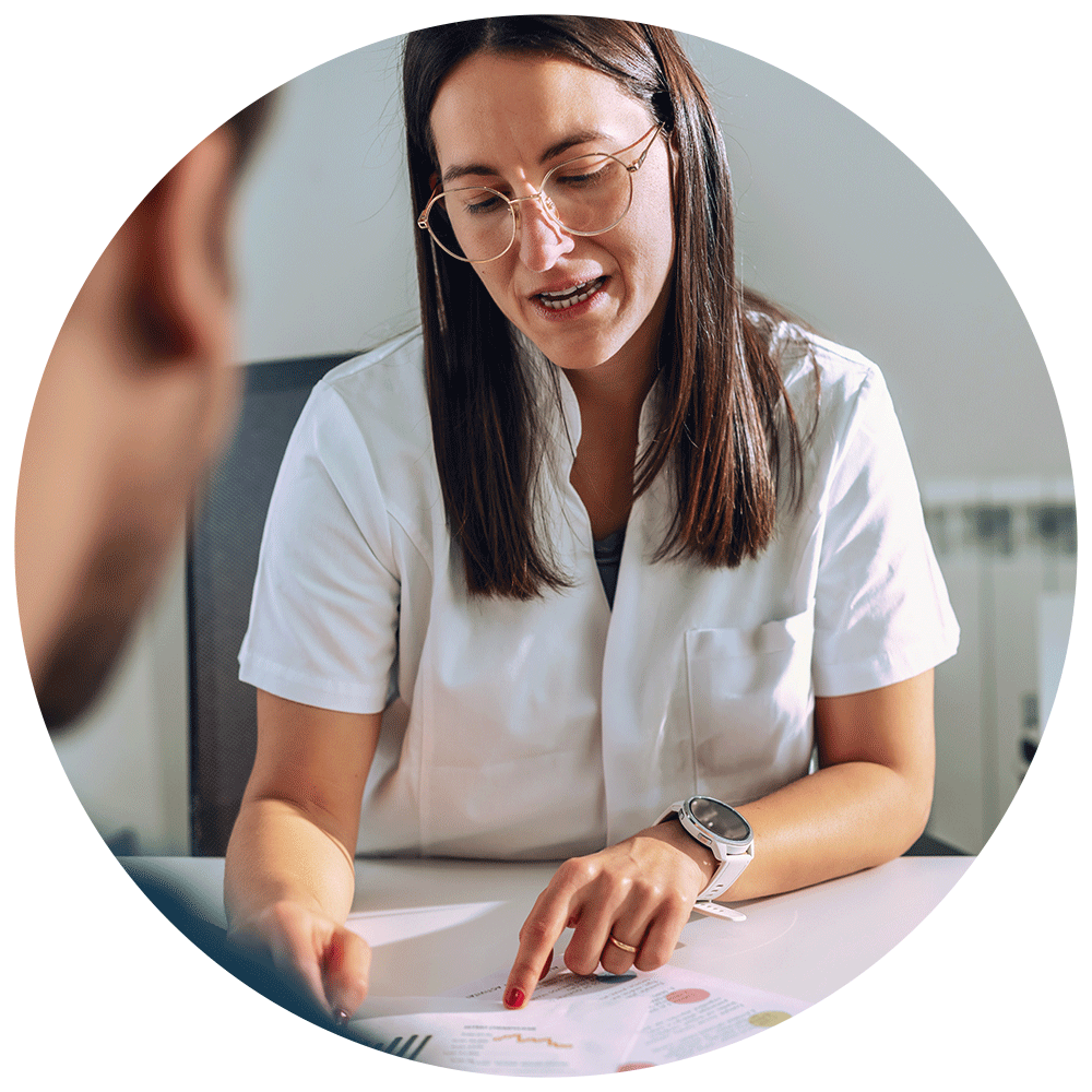 Female nutritionist in white uniform reviews dietary charts with patient across table.